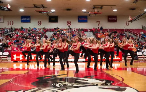 Wide angle photo of the dance team at center court doing a routine during halftime of a men's basketball game.