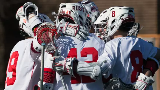 Five men's lacrosse players huddle together to celebrate a goal