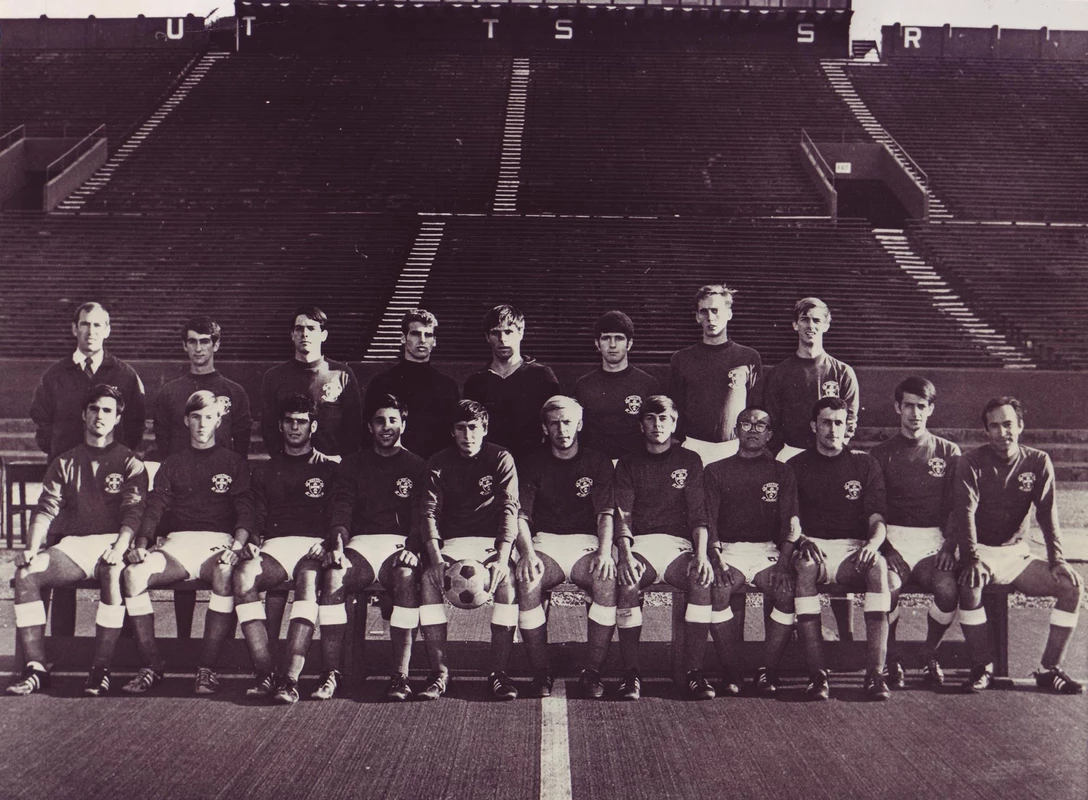 1968 Boston University men's soccer team photo with 11 players sitting and seven players plus the head coach standing behind them. The team photo was taken at Nickerson Field in front of the stands.