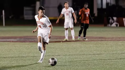 Ryan Lee takes a hard shot toward the goal with player from both teams looking on in the background.