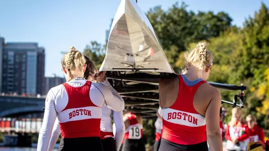 BU women's rowers carry a boat on the dock.