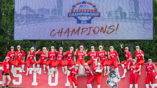 Members of the Boston University softball team pose for a group photo in front of the video board celebrating the Patriot League championship victory.