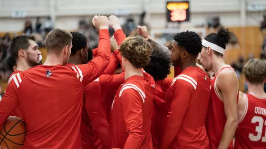 BU men's basketball has a group huddle at Hartford with fists meeting in the middle.