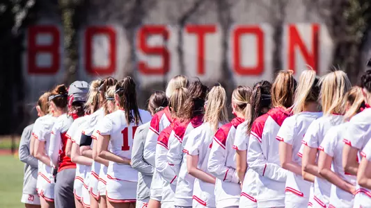 The women's lacrosse team lines up for the national anthem in front of the BU ivy facade.