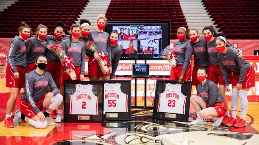 The players of the women's basketball team huddled around each other with senior day jerseys in the middle
