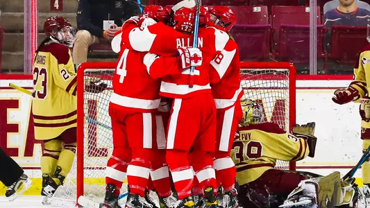 The women's ice hockey team celebrates their game-winning goal in front of the Boston College net