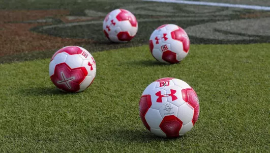 Four BU branded soccer balls in the middle of the field