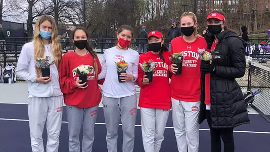 Katya Martens, Alex Angyalosy, Lily Burchell, Emily Kim, Dani Blaser and Mia Wallace are standing next to each other masked while holding flowers in an intimate Senior Day ceremony at Holy Cross.