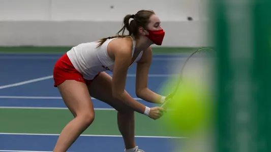 A women's tennis player is crouching over ready for a doubles volley as she gets set near the tennis net.