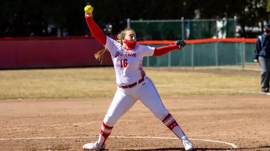 Ali DuBois is in the middle of her pitching windup with the ball up high above her head before throwing toward home plate.