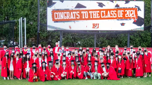 The Class of 2021 poses for a photo in front of the BU Softball Field video board, which displays a message congratulating the Class of 2021