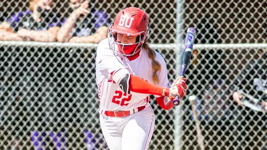 Caitlin Coker is in mid swing at home plate as the pitch comes toward her. She's batting left handed.