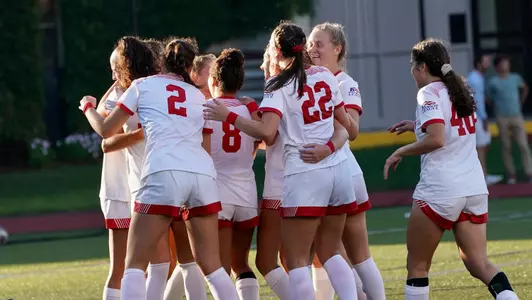 Women's soccer celebrates a goal with a big group hug.