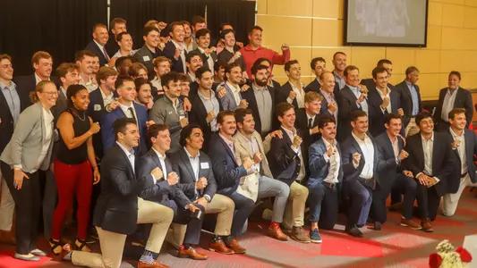 The 2022 men's lacrosse team and staff pose with their Patriot League championship rings at a team banquet