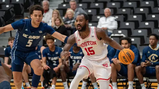 Jonas Harper handles the ball in front of the UC Davis bench with a defender to his side.