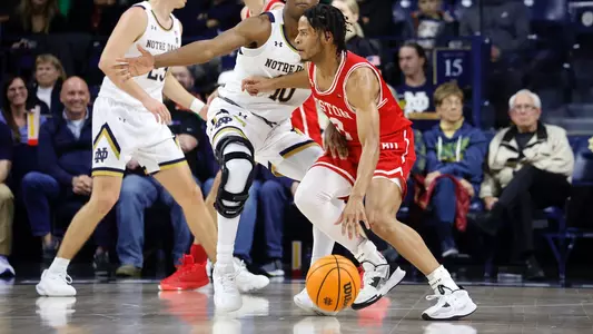 Ethan Brittain-Watts dribbles with a Notre Dame defender to the side guarding him from reaching the hoop.