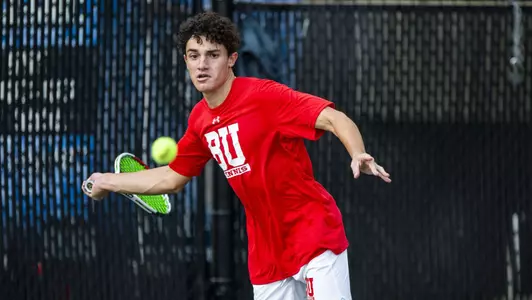 Dion Loutas moves to his right to hit a forehand on a tennis ball hanging in the air.