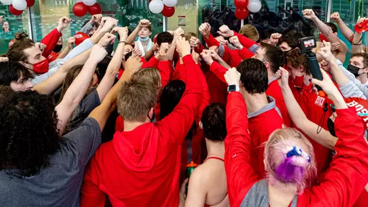 The entire BU swimming & diving team gather into a big huddle with their fists raised toward the middle.
