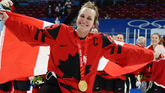 Marie-Philip Poulin wearing a gold medal and holding the Canadian flag behind her