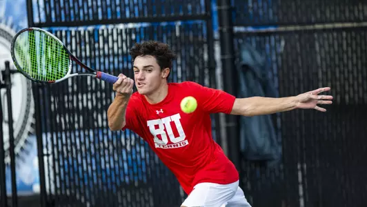 Dion Loutas makes a leaping forehand hit on a tennis ball with outstretched arm.