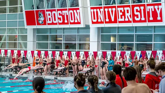 Student-athletes watch teammates compete in the pool from the side.