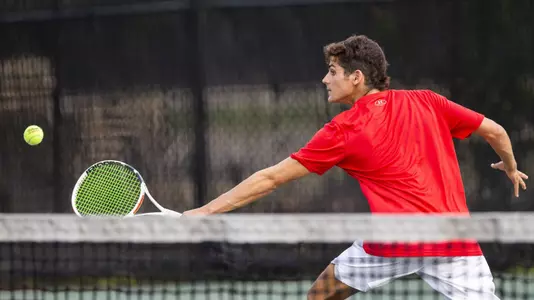 Jonah Dickson goes for a backhand volley with the racquet in his left hand as he lunges to the side.