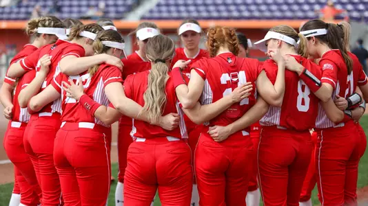 Boston University softball team huddles in a circle with arms around each other.