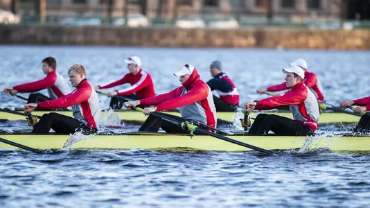 Two Boston University men's rowing varsity eight boats race down the Charles River side by side.