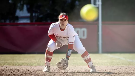Nicole Amodio is crouched at first base in a defensive position waiting for the hit ball to approach.