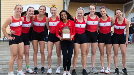 BU women's lightweight rowing varsity eight boat members pose for a group photo with the Beanpot.