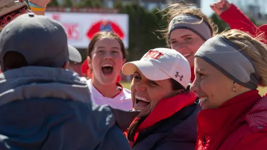 BU Softball team celebrates head coach Ashley Waters winning her 200th career game. They're in a semi huddle with the players and coach laughing/cheering.