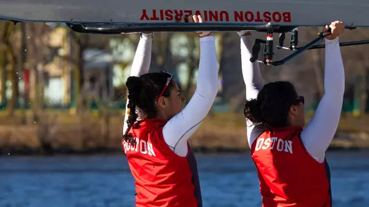 BU women's rowers carry a boat on the dock.