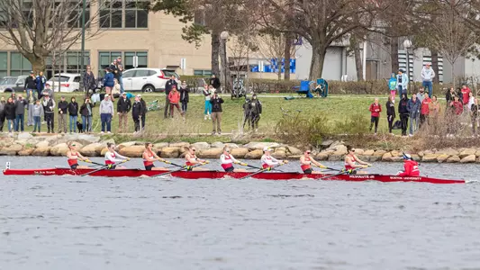 Lightweight boat rows down the Charles River toward the finish line with fans looking.