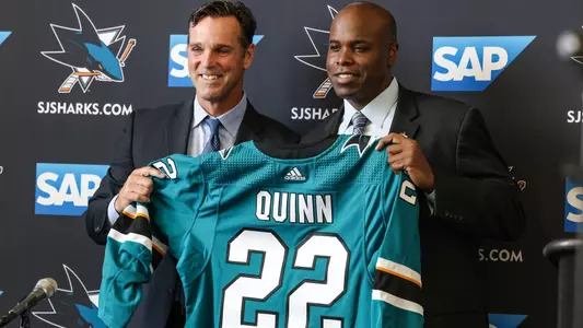 David Quinn and Mike Grier hold a San Jose Sharks jersey with Quinn and the number 22 on the back at the press conference introducing Quinn as head coach of the Sharks