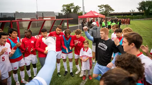 Men's Soccer Team gathers in a circle and starts raising fists while closing the huddle.
