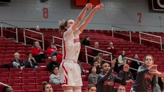 Photo of women's basketball senior Liz Shean shooting a three-pointer while the Terrier bench looks on.