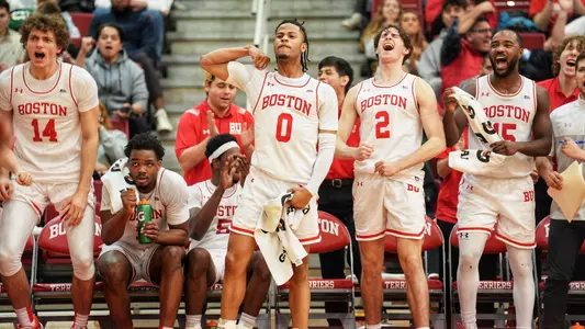 Members of BU men's basketball bench jump up and scream or clap in celebration after a play is made.