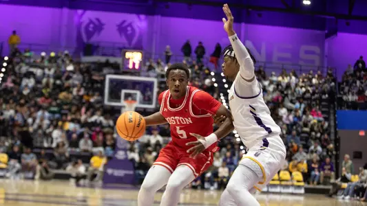 Kyrone Alexander dribbles the ball toward the hoop with a UAlbany defender on his back.