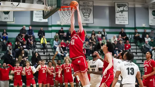 Otto Landrum leaps up for a slam dunk at Wagner with his teammates on the bench standing up.