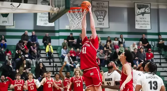 Otto Landrum leaps up for a slam dunk at Wagner with his teammates on the bench standing up.