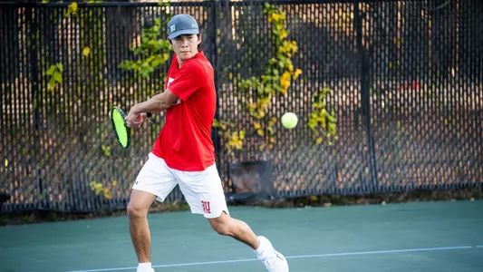 Corey Craig holds the racquet back during a backhand swing as the tennis ball approaches.