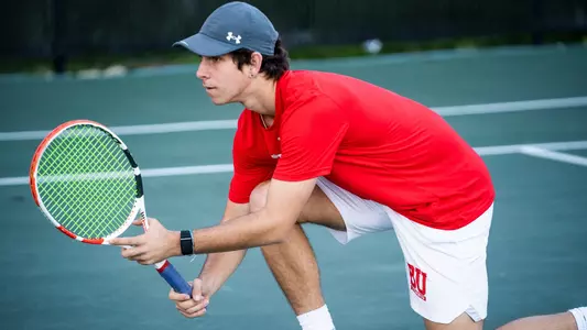 Adrian Pawlowski crouches on one knee in front of the net awaiting a serve during doubles play.