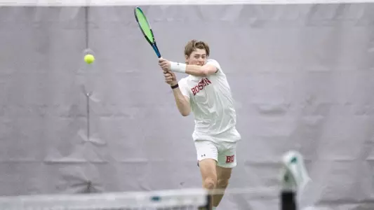Cole Knutsen uses a double backhand to hit the tennis ball over the net.