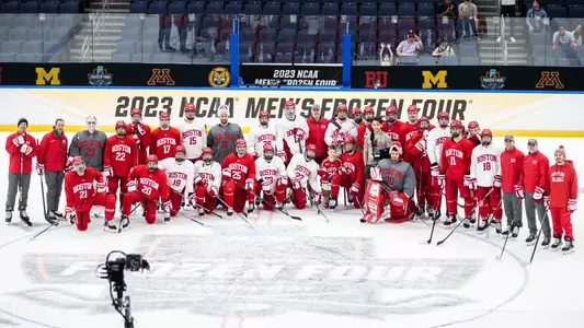 The men's ice hockey team takes a photo at the center ice Frozen Four logo