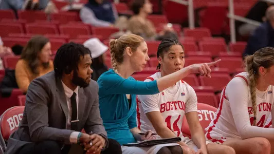 Photo of women's basketball coach Brianna Finch (middle left) instructing Sydney Johnson on the bench.