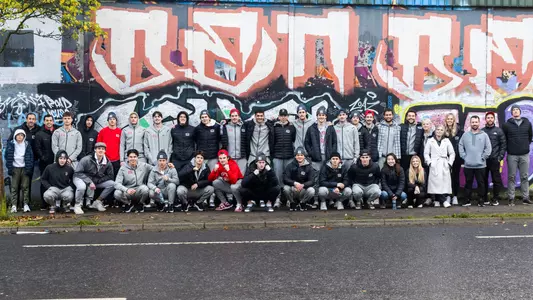BU men's ice hockey players and staff pose in front of the Belfast Peace Wall