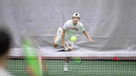 Johann Sajonz hits a serve over the tennis net while leaping forward