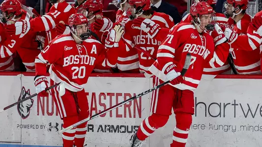 Lane Hutson skating behind Macklin Celebrini as they both high five the BU bench after a goal