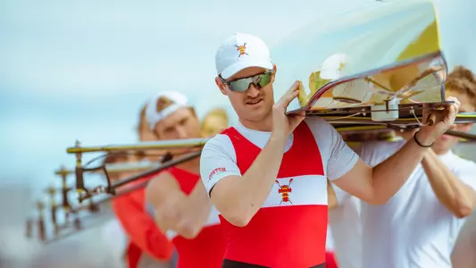 Photo of men's rower Bowen de Gouw helping the BU crew place the boat in the water during the Head of the Charles.
