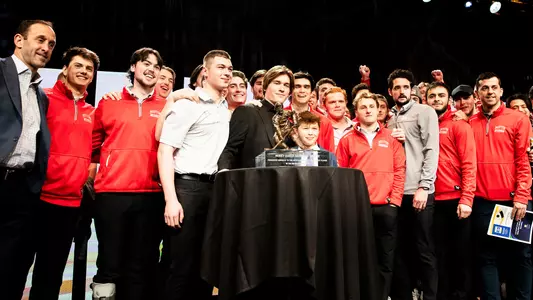 Macklin Celebrini poses for a photo with the Hobey Baker trophy and his teammates and coaches